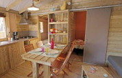 Interieur van een knusse houten lodge met keuken, eethoek en uitzicht op slaapkamer in Mas de Champel, Frankrijk.