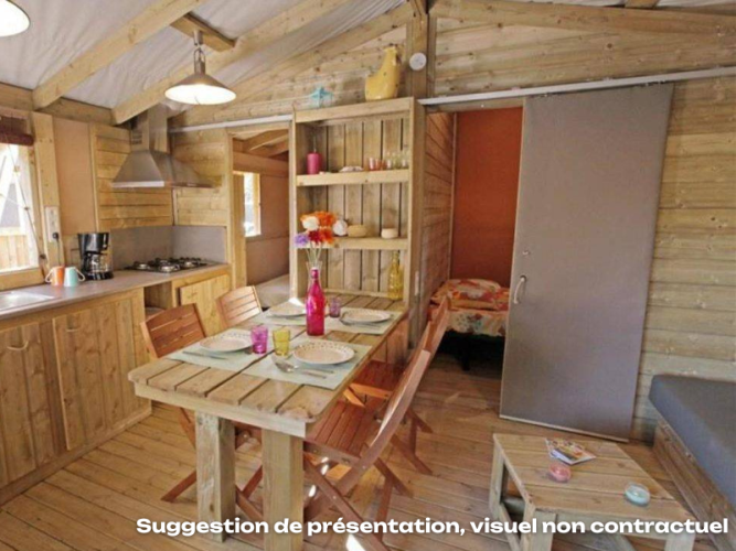 Interieur van een knusse houten lodge met keuken, eethoek en uitzicht op slaapkamer in Mas de Champel, Frankrijk.