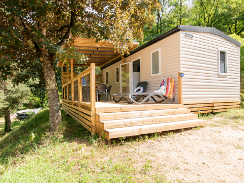 Casa móvil moderna con terraza de madera y tumbonas, rodeada de árboles y naturaleza para descansar.