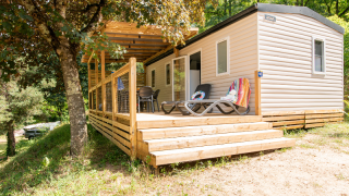 Stacaravan met houten terras en ligbedden, gelegen in een bosrijke, groene omgeving voor ontspanning.
