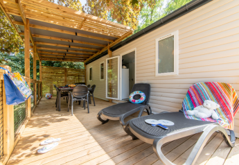Veranda in legno di una casa mobile con lettini, tavolo da pranzo e atmosfera estiva rilassante.