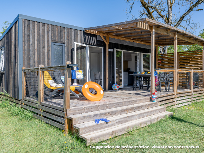 Außenansicht der Homeflower Premium-Lodge mit Holzterrasse, Liegen, Spielsachen und Garten im Sonnenschein.