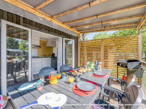 Espace repas extérieur dans un hébergement glamping avec table dressée et vue sur cuisine moderne.
