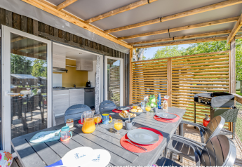 Buiteneethoek bij een glampingaccommodatie met gedekte tafel en zicht op moderne keuken binnen.