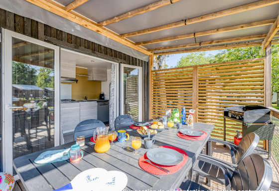 Espace repas extérieur dans un hébergement glamping avec table dressée et vue sur cuisine moderne.