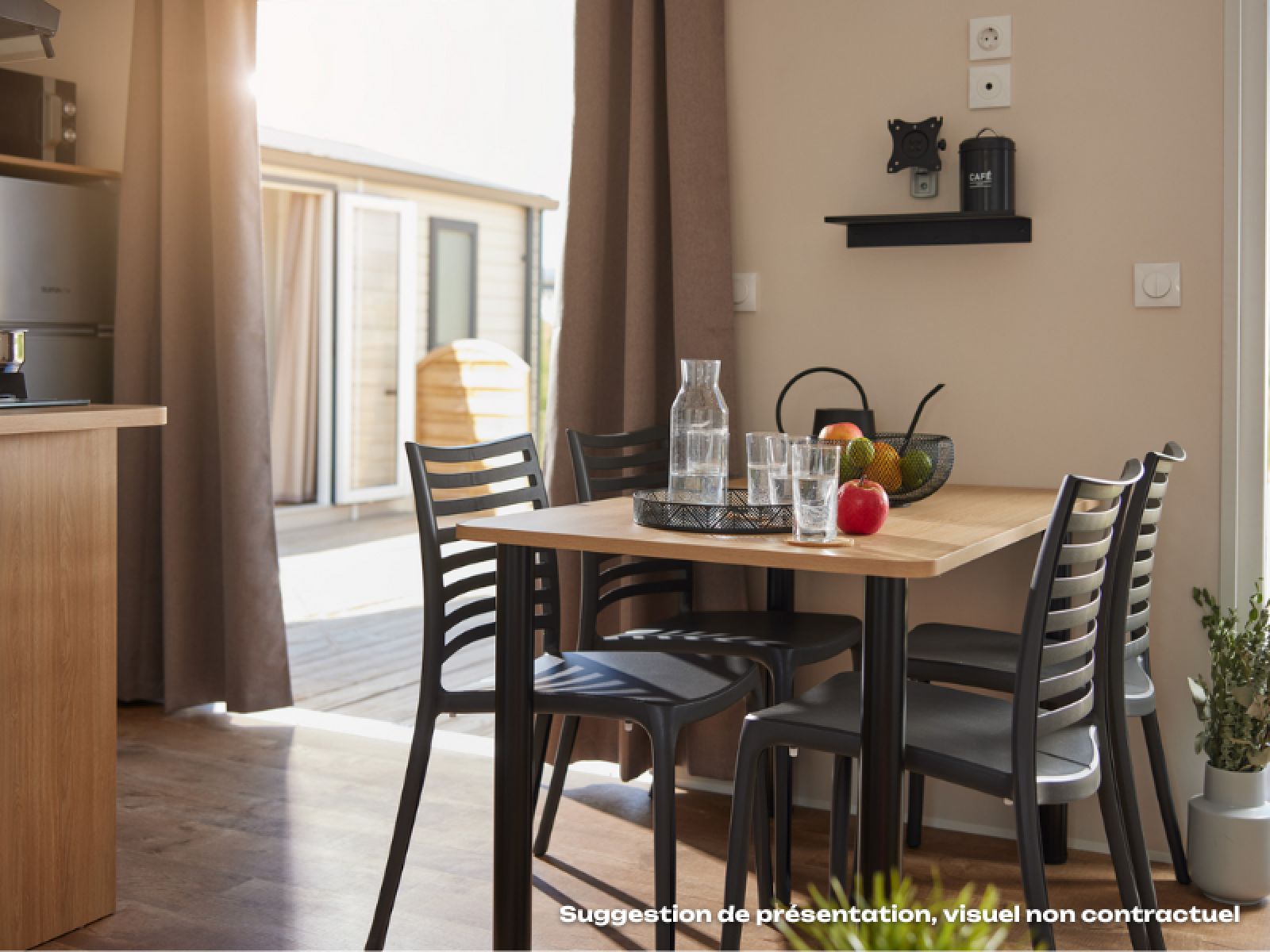 Eethoek binnen in een glamping-accommodatie met houten tafel, vier stoelen en een fruitschaal op tafel.