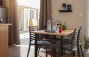 Eethoek binnen in een glamping-accommodatie met houten tafel, vier stoelen en een fruitschaal op tafel.