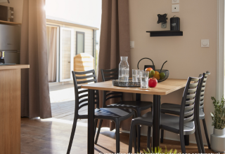 Coin repas intérieur dans un hébergement glamping avec table en bois, quatre chaises et corbeille à fruits.