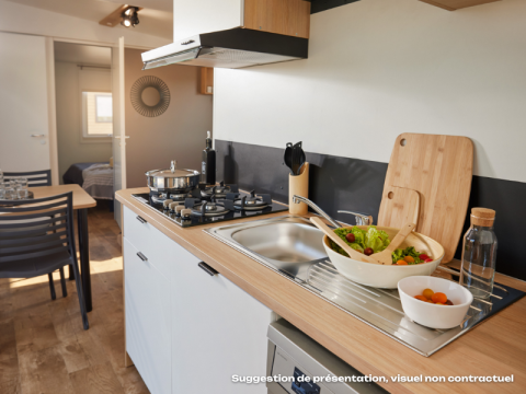 Moderne glampingkeuken met houten werkblad, gasfornuis, salade en zicht op eet- en slaapkamer.