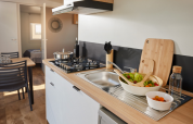 Moderne glampingkeuken met houten aanrecht, gasfornuis, saladekom, eethoek en zicht op de slaapkamer.