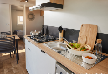 Modern glamping kitchen with gas stove, wooden countertop, salad bowl, dining area, and bedroom in view.