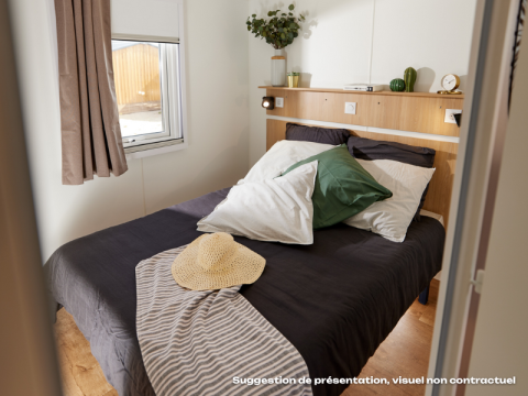 Gezellige glamping slaapkamer met dubbel bed, kussens, planten en natuurlijk licht via het raam.