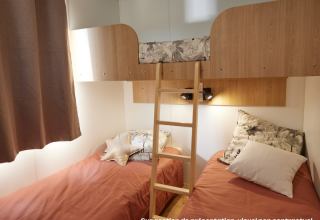 Chambre de glamping avec deux lits simples, un lit superposé en haut et une échelle en bois au centre.