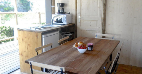 Cuisine et table à manger dans une tente safari avec meubles en bois, appareils et bol de fruits.