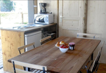 Cuisine et table à manger dans une tente safari avec meubles en bois, appareils et bol de fruits.