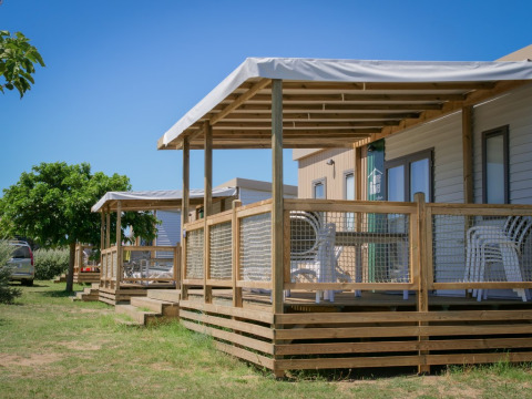 Buitenzicht op Homeflower Premium-hutten met houten terrassen en stoelen onder een zonnige hemel.
