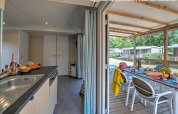 Innenaufnahme einer Kabine mit Küche, offen zur überdachten Terrasse und gedecktem Tisch im Freien.