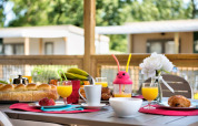 Frühstück auf einer Terrassenhütte mit Saft, Gebäck, Brötchen und einer weißen Blume in einer Vase.