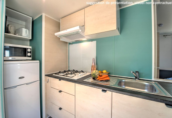 Heldere compacte keuken in een cabine met gasfornuis, spoelbak, koelkast en verse groenten en fruit.