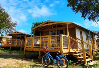 Lodge Sweetflower op palen Premium con veranda in legno, bici blu davanti e cielo azzurro limpido sopra.