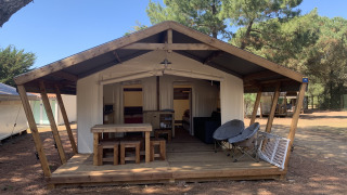 Tenda safari Freeflower Standaard con veranda in legno, tavolo da picnic e sedie tra pini all'aperto.