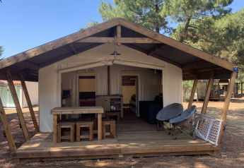 Safari-tent Freeflower Standaard met houten terras, picknicktafel en stoelen in een bosrijke omgeving.
