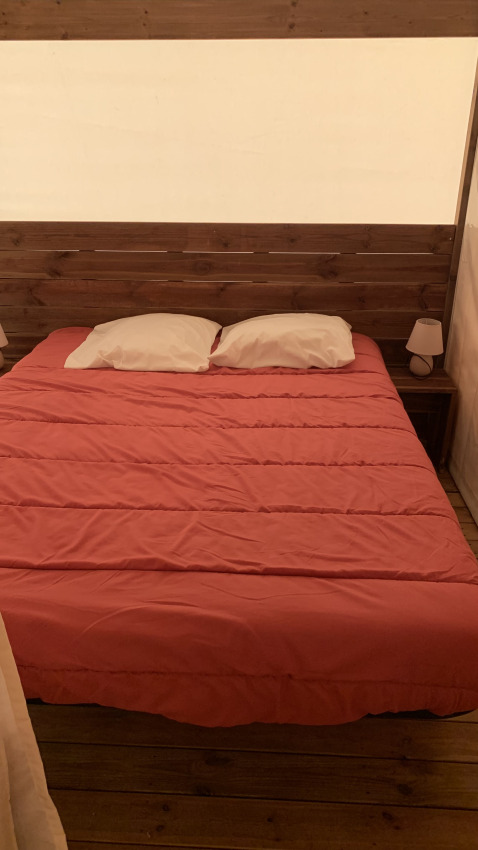 Bed met rood dekbed en twee witte kussens in een safaritent bij Flower Camping Le Bel Air, Frankrijk.