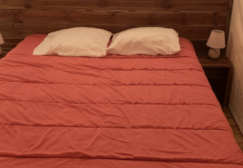 Letto con copriletto rosso e due cuscini bianchi in una tenda safari al Flower Camping Le Bel Air, Francia.