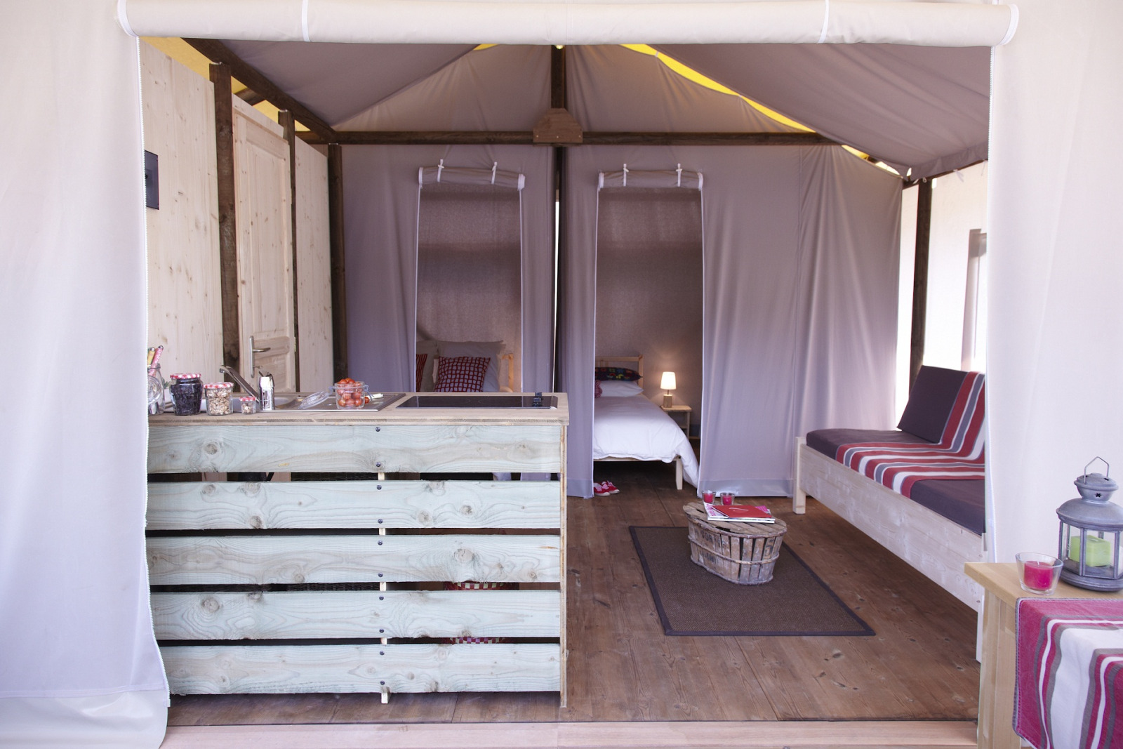 Interieur van safari tent Hut lodge op heipalen Standaard bij Flower Camping Le Bel Air in Frankrijk, met bed en bank.