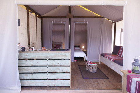 Innenraum des Safari-Zeltes Hut lodge op heipalen Standaard bei Flower Camping Le Bel Air in Frankreich mit Bett und Sofa.