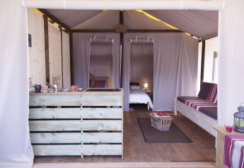 Interiør af safari teltet Hut lodge op heipalen Standaard på Flower Camping Le Bel Air i Frankrig, med seng og sofa.