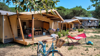 Safari-Zelt Ecolodge Cotton Comfort mit Terrasse, Fahrrad und Liegestuhl auf einem sonnigen Campingplatz.