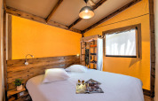 Schlafzimmer im Blokhut Cotton Comfort Safarizelt auf Flower Camping Le Bel Air mit Holzbett und Fenster.