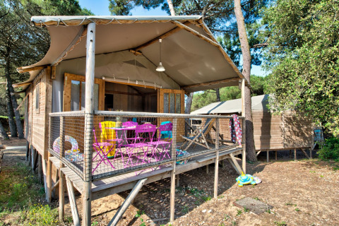 Vista esterna della Hut Lodge hout Comfort, con sedie colorate e giocattoli per bambini sul terrazzo in legno