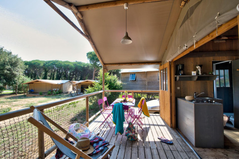 Vista del porche del Hut Lodge Comfort en Flower Camping Le Bel Air, Francia, con comedor exterior y cocina.