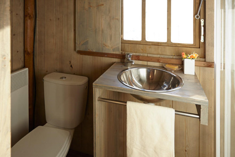 Bagno con pareti in legno, lavabo in acciaio, wc, asciugamano e finestra in una baita di Le Bel Air.