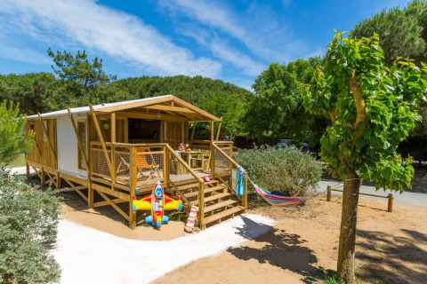 Safari tent Sweetflower Premium met houten terras, hangmat en kinderspeelgoed, tussen groen en zon.