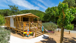Safari tent Sweetflower Premium met houten terras, hangmat en kinderspeelgoed, tussen groen en zon.