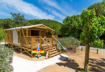 Safari tent Sweetflower Premium met houten terras, hangmat en kinderspeelgoed, tussen groen en zon.