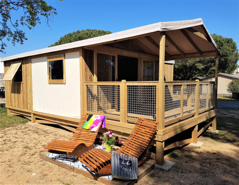 Cosyflower Premium blokhut met houten terras, ligstoelen en bloemen, omgeven door natuur.