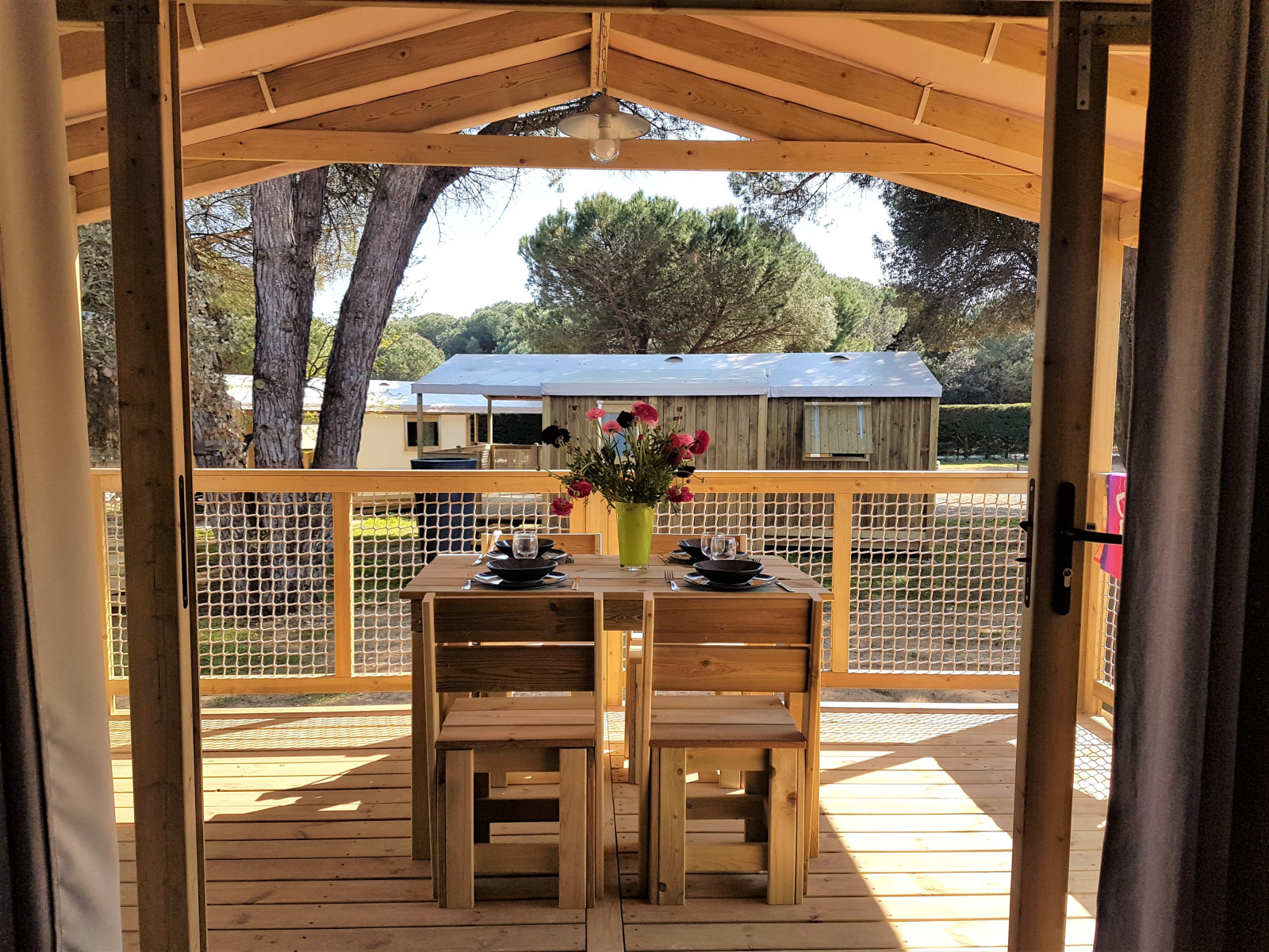 Uitzicht vanuit de Cosyflower Premium cabin bij Flower Camping Le Bel Air met houten terras en gedekte tafel.