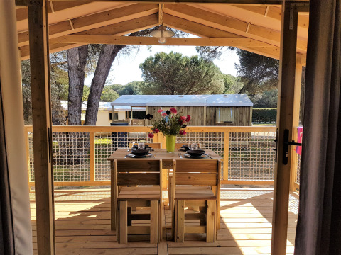 Zicht vanuit de Cosyflower Premium hut op Flower Camping Le Bel Air met houten terras en eettafel buiten.