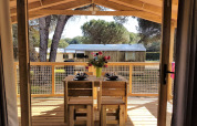 Zicht vanuit de Cosyflower Premium hut op Flower Camping Le Bel Air met houten terras en eettafel buiten.