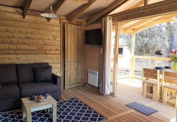 Indvendigt billede af en hyggelig træhytte, Cosyflower Premium, med sofa og spiseplads ved Flower Camping Le Bel Air.