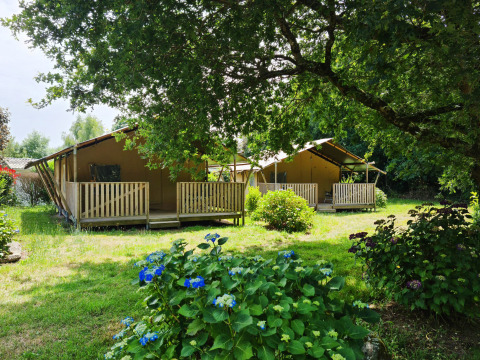 Deux tentes safari avec terrasses en bois au Flower Camping Le Kerleyou en France, entourées de verdure et de fleurs.