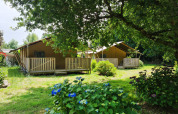 Twee safaritenten met houten veranda’s op Flower Camping Le Kerleyou in Frankrijk, omgeven door groen en bloemen.