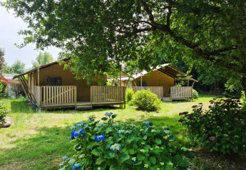 Due tende safari con verande in legno al Flower Camping Le Kerleyou in Francia, circondate da piante e fiori.