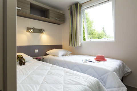Helles Glamping-Zimmer mit zwei Einzelbetten, offenem Fenster, Spielzeug und rosa Hut auf dem Bett.