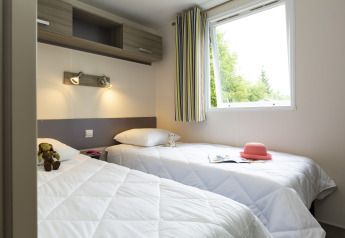 Helles Glamping-Zimmer mit zwei Einzelbetten, offenem Fenster, Spielzeug und rosa Hut auf dem Bett.