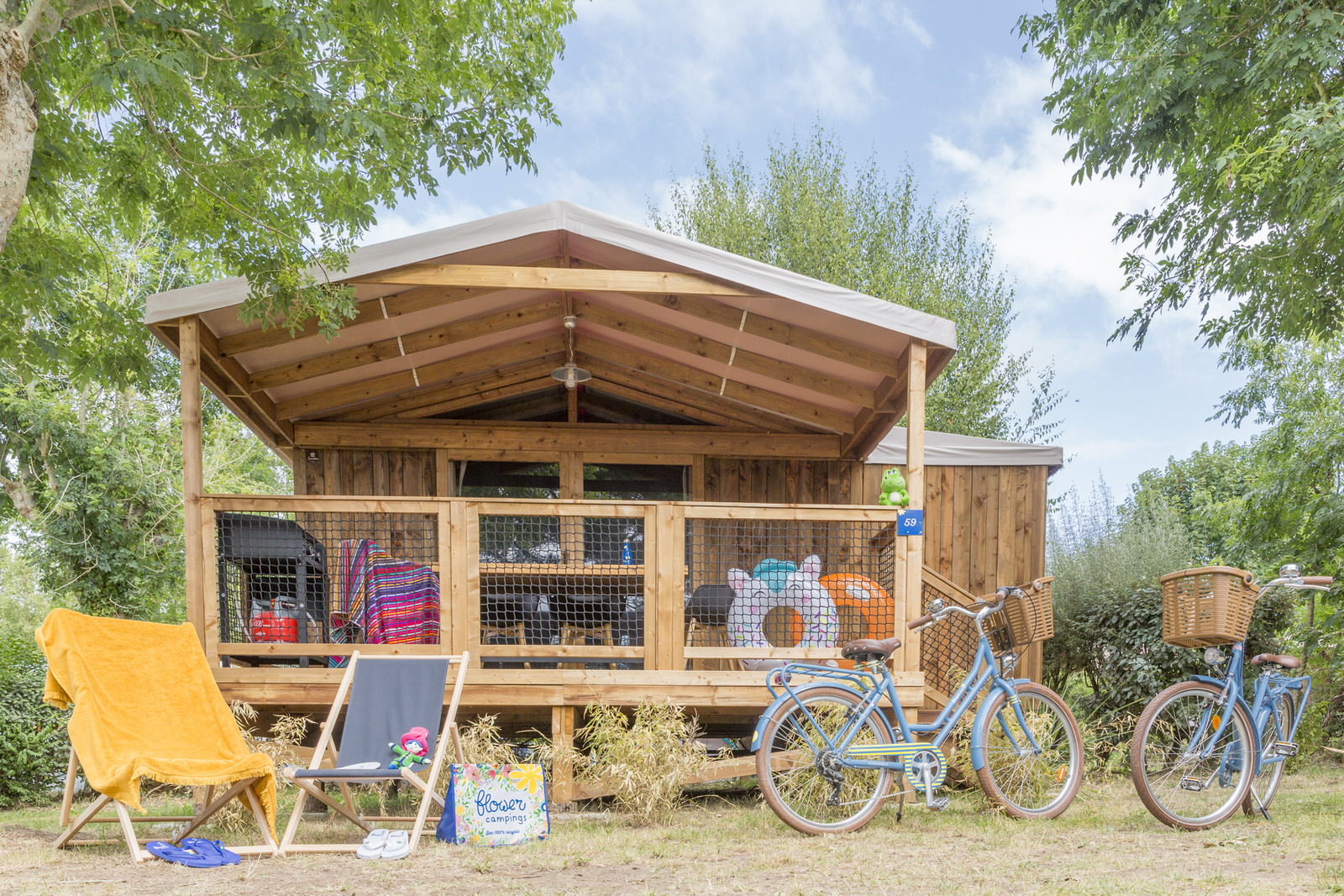 Cosyflower Premium blokhut met overdekte veranda, ligstoelen, fietsen en kleurrijke zomerspullen buiten.